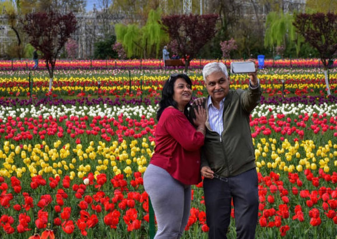 SRINAGAR, KASHMIR, INDIA - 2023/04/04: An Indian tourist couple takes a selfie at the Asia's largest tulip garden during a cloudy spring day. Despite the inclement weather, tourists are flocking the famed Tulip garden in Srinagar. Officials claim that over 100,000 tourists have visited the garden within the first ten days of its opening. 1.6 million tulips are in full bloom at the worlds largest garden situated at the banks of Dal lake. (Photo by Saqib Majeed/SOPA Images/LightRocket via Getty Images)